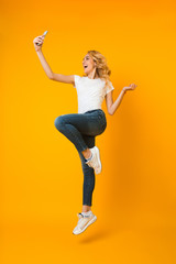 Fototapeta na wymiar Overjoyed woman jumping and taking selfie on phone