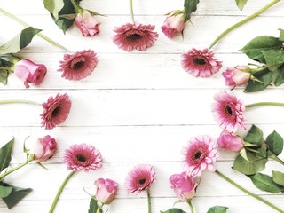 Flowers composition. Frame made of pink rose and gerbera flowers on white wooden background. Flat lay, top view, copy space.