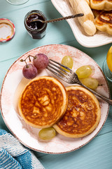 Healthy breakfast with fresh hot pancakes with berry jam and fruits on turquoise background, top view, flat lay. Food concept.