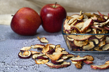 Dried Apple chips in a square glass plate and two red apples on a gray concrete background. Organic natural food. side view