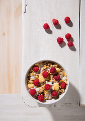 Bowl of granola with yogurt and raspberry on a white wooden background