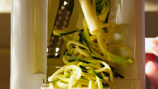 Spiralizing zucchini noodles into zoodles. Handheld crank turns the squash into long strands of gluten free pasta alternative. The delicious vegetable is perfect for vegan lifestyles, paleo cooking an