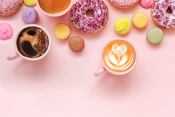 Obraz na płótnie Canvas Coffee cups, delicious pink donuts with sprinkle and colorful bright macaroons on pink paper background