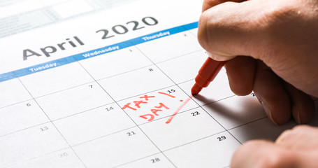 Writing tax day on 2020 April 15 calendar with red marker. Deadline for 1040 form return.