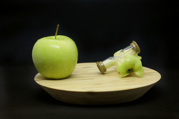 Green apple, sandglass and apple core on a wooden plate isolated on a black background.