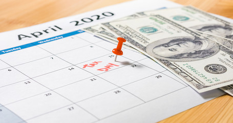 Red pin marked at April 15 for tax day with dollars falling on 2020 calendar.