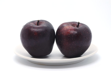 Two dark red apples on a light plate isolated on a white background.