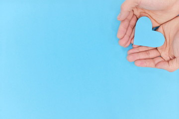 Hands holding a blue heart in blue background. Top view with copy space.