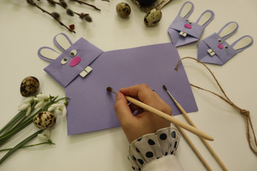The child's hand draws on a postcard in the form of a hare on the background of willow branches and eggs