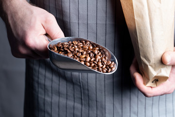 A man pours coffee beans into a paper bag with a metal scoop.