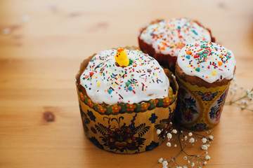 Homemade easter cakes with colorful sprinkles on rustic wooden table with white flowers. Happy Easter. Traditional Easter bread. Copy space