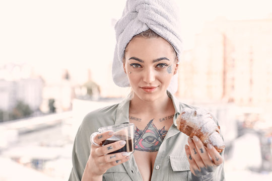 Home Leisure. Young woman in underwear and towel standing on balcony with cup of coffee and croissant smiling playful close-up