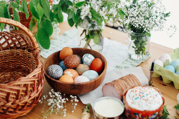 Easter eggs natural dyed, easter bread cake, ham, butter, green branches  and flowers on rustic wooden table with wicker basket and candle. Traditional Easter Food for blessing in church