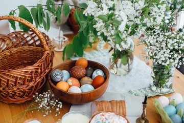 Easter eggs natural dyed, easter bread cake, ham, butter, green branches  and flowers on rustic wooden table with wicker basket and candle. Traditional Easter Food for blessing in church