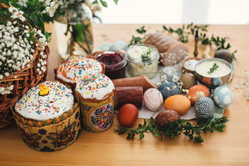 Easter brunch.  Easter modern eggs, easter bread, ham, beets, butter, cheese, sausages, green branches and flowers on rustic wooden table. Holiday preparation. Traditional Easter Food.