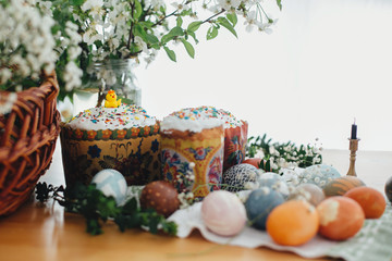 Fototapeta na wymiar Traditional Easter food on rustic table. Homemade easter cake, easter eggs natural dyed, candle, green branches and flowers with wicker basket on wooden background. Easter Food for sanctify