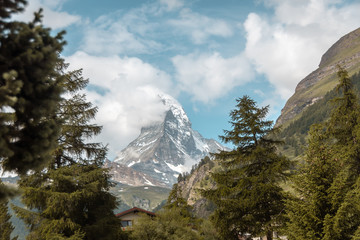 Matterhorn in clouds and traditional wooden houses and farm buildings on the slope. Zermatt, Swiss...