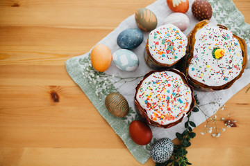 Homemade easter cake and stylish easter eggs natural dyed on rustic cloth with flowers and green brunches on wooden table. Happy Easter. Traditional Easter bread. Flat lay