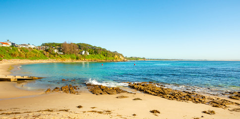 A scenic wide angle landscape view of a beautiful calm beach in NSW, Australia on a stunning day with blue sky