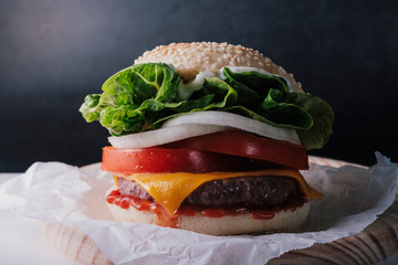 front view of fresh tasty burger on wood table with dark background