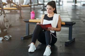 Attractive woman with notebook planning her workout schedule in sports club