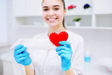 a woman doctor holds a red heart and a paper printout of a cardiogram. Prevention of cardiovascular...