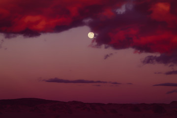 Abstract landscape. Night scene. Dramatic cloudy sky in red colors, and bright Moon.