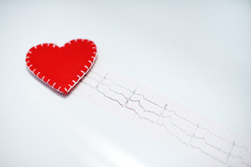 red felt heart on the background of a paper printout of an ECG chart or an electrocardiogram on a...
