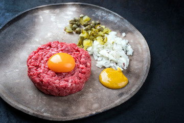 Gourmet tartar raw from beef fillet with yellow of the egg, gherkin and capers as closeup on a modern design rustic plate