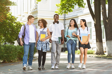 Happy university students walking together on campus, chatting and laughing outdoors