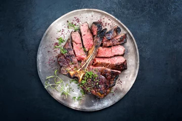 Tuinposter Barbecue dry aged wagyu porterhouse beef steak sliced with large fillet piece with herbs and red salt as top view on a modern design rustic plate with copy space © HLPhoto