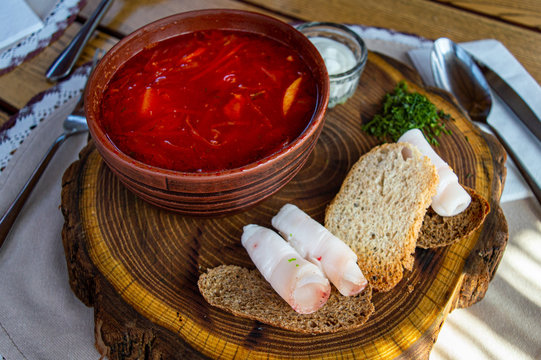 Beet soup in ceramic plate with becon, bread and sour cream on wooden board. Borch, traditional Ukrainian food
