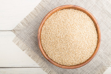 Wooden bowl with raw white quinoa seeds on a white wooden background. Top view, close up.