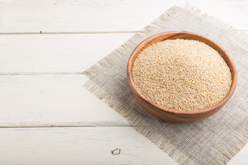 Wooden bowl with raw white quinoa seeds on a white wooden background. Side view, copy space.