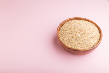 Wooden bowl with raw white quinoa seeds on a pastel pink background.  Side view, copy space.