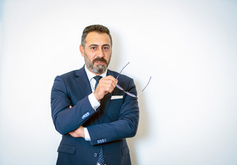 Naklejka premium A bearded businessman posing with his glasses in his hands in a suit in front of the background