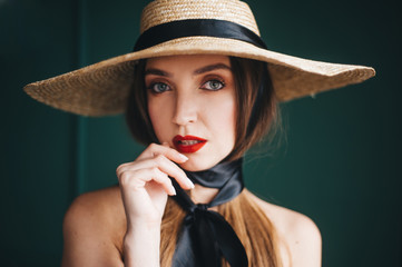 Beautiful woman in a straw hat with black ribbons on a green background.