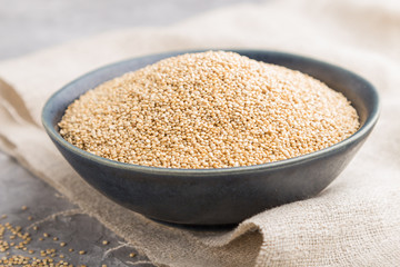 Blue ceramic bowl with raw white quinoa seeds on a gray concrete  background. Side view, selective focus.