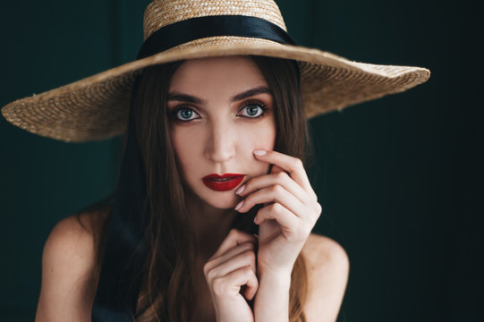 Beautiful Woman In A Straw Hat With Black Ribbons On A Green Background.