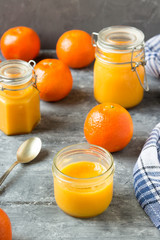 Homemade tangerine jam in glass jars and fresh tangerines on a wooden table. Location vertical.