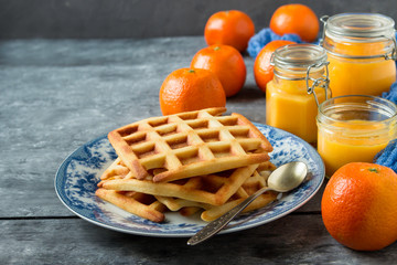 Homemade belgian waffles with tangerine jam and fresh tangerines on the table. The horizontal location.