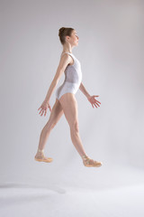 Young woman ballet dancer in white leotard leaping in studio.