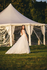 Beautiful young woman in a white wedding dress and black boots at sunset is photographed.