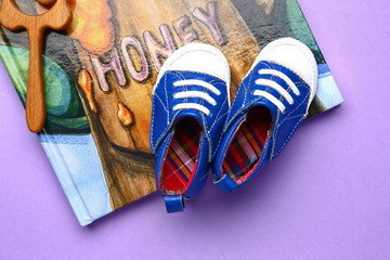 Baby booties with toy and book on color background