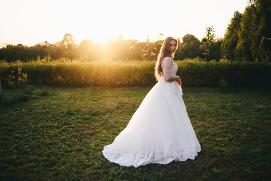 Beautiful young woman in a white wedding dress and black boots at sunset is photographed.