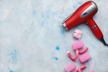 Modern hair dryer and curlers on light background