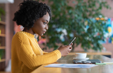 Concentrated black girl using smartphone at cafe