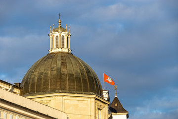 Vilnius, Lithuania - March 2, 2019: Dome of the Casimir Chapel of Cathedral Basilica. Behind it - a fragment of the Palace of the Grand Dukes of Lithuania with State flag. In the sky background
