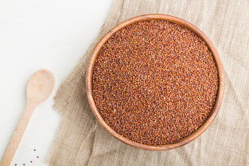 Wooden bowl with raw red quinoa seeds on a white wooden background. Top view, close up.