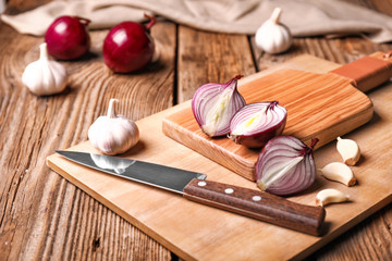 Fresh raw onion, garlic, cutting board and knife on wooden background